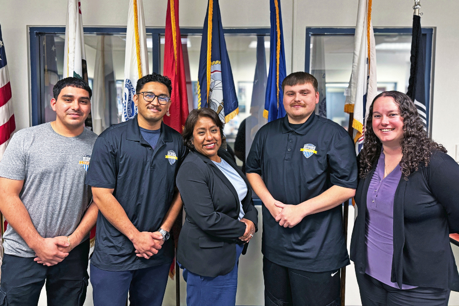 group of students and staff standing in the veterans success center near military service flags