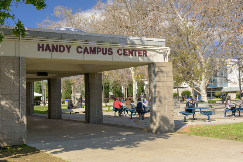 eastside entry of the Handy Campus Center looking northwest, showing students at the outdoor patio seating area with the Hayden Memorial Library behind them
