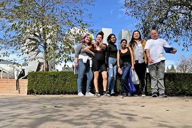rising scholars students stand together on a campus walkway near large outdoor letters under a blue sky