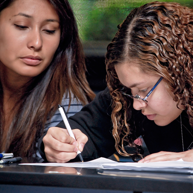 two female citrus college students in a classroom setting taking notes