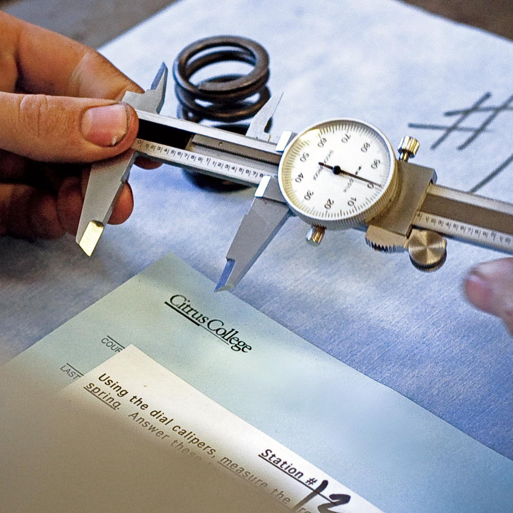 student hands use dial calipers to measure a metal spring during a citrus college technical exercise