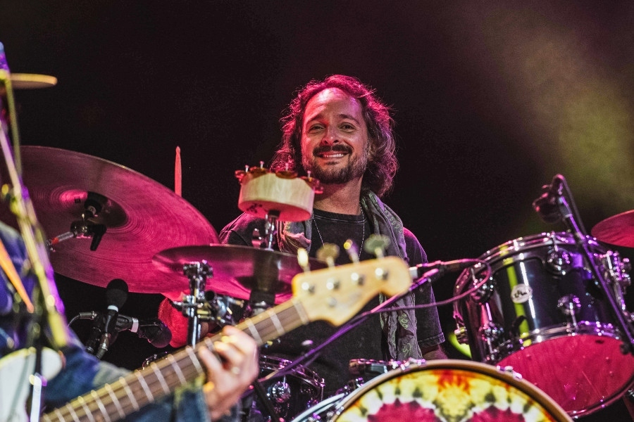 anthony logerfo smiles while performing on drums under colorful stage lighting