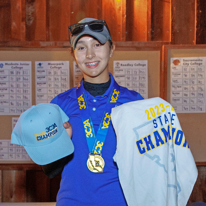 isabelle olivas-lowell displays her 3c2a state champion medal, hat and shirt after winning the women's golf title