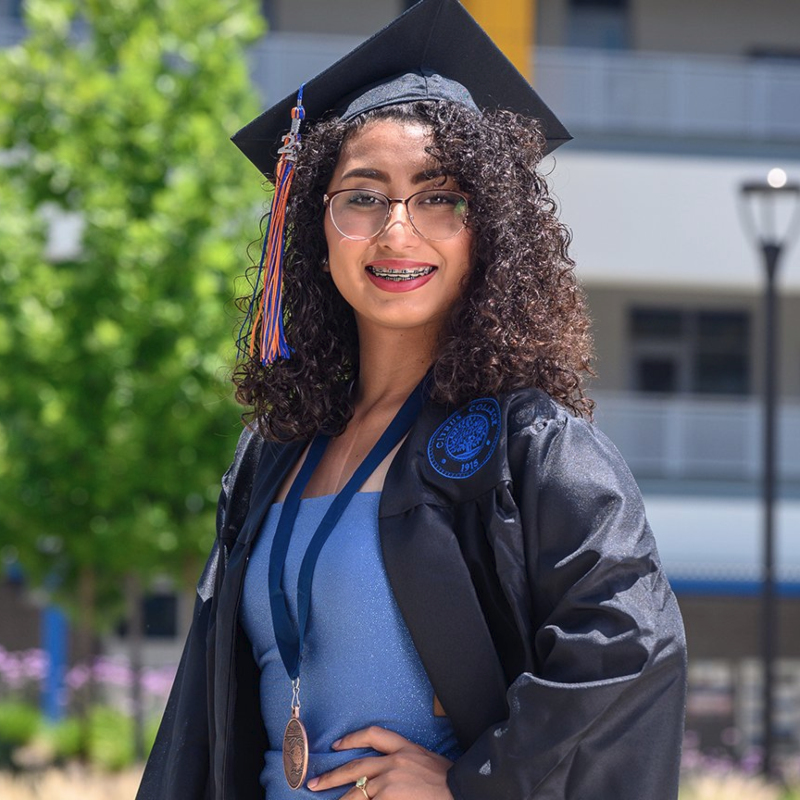 Jennifer Castaneda poses in front of the college's ED Building in her graduation cap and gown