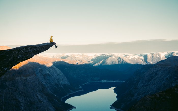 Adventurous man sitting on top of the Trolltunga rocky cliff.